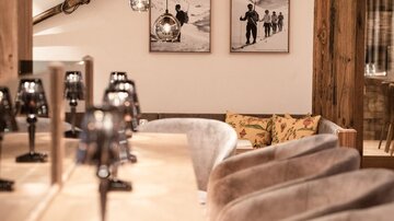Ein gemütlicher, moderner Innenraum mit einer Theke und eleganten Stühlen. An den Wänden hängen Bilder von Menschen in den Bergen.