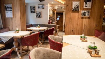 Ein gemütliches Restaurant mit Holzwänden und roten Stühlen. Auf den Tischen stehen kleine Pflanzen und Kerzen.