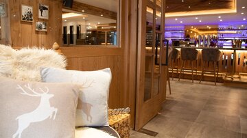 Ein modernes Restaurant mit warmem Holzdesign und stilvollen Barhockern. Auf dem Sofa liegen gemütliche Kissen mit einem Hirschmotiv.