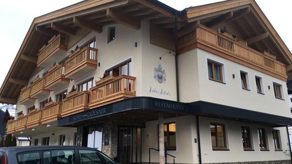 Ein modernes Gebäude mit mehreren Balkonen und einem Restaurant. Die Fassade ist in hellem Farbton gestaltet, umgeben von einem Parkplatz.