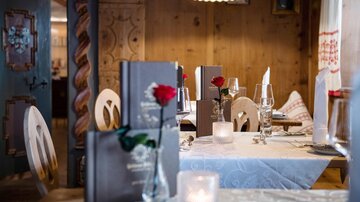 Ein gemütliches Restaurant mit Holzinterieur und elegant gedeckten Tischen. Auf den Tischdecken liegen Menükarten, Kerzen und rote Rosen.