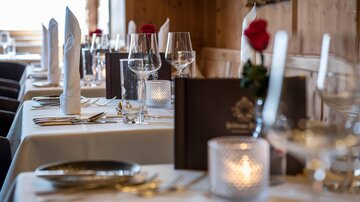 Ein elegant gedeckter Tisch in einem Restaurant. Die Tischdeko umfasst weiße Servietten, Gläser und rote Rosen.
