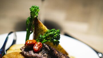 Ein köstlicher Teller mit gegrilltem Steak, einem Schnitzel und buntem Gemüse. Dazu gibt es ein Glas Rotwein im Hintergrund.