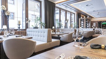 Ein elegantes Restaurant mit hellen Fensterfronten und modernen Möbeln. Der Tisch ist liebevoll gedeckt und der Raum wirkt einladend.
