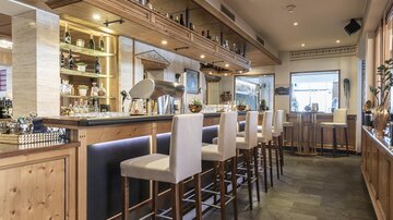 Ein eleganter Barbereich mit Holzverkleidung und modernen Barhockern. Der Raum ist gut beleuchtet und bietet eine einladende Atmosphäre.