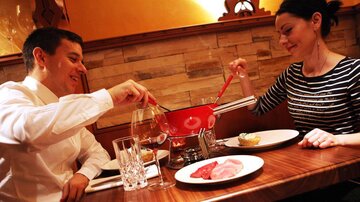 Ein Paar genießt ein Fondue-Dinner in einem gemütlichen Restaurant. Auf dem Tisch stehen verschiedene Zutaten und Gläser Wein.