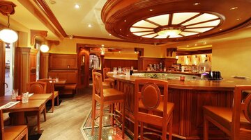 Eine elegante Bar mit Holzinterieur und einer einladenden Atmosphäre. Hochstühle und Tische laden zum Verweilen ein.