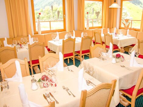 An elegant dining room with set tables and festive decoration. Large windows provide a view of the surrounding landscape.