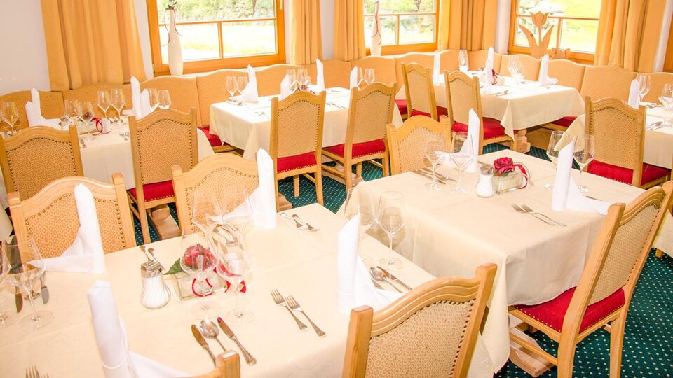 An elegant dining room with set tables and festive decoration. Large windows provide a view of the surrounding landscape.
