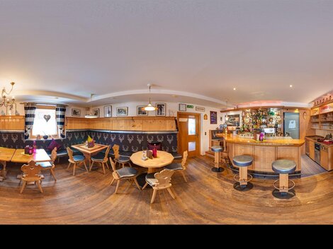 A cozy bar with wooden furniture and tables. The walls are decorated and there is a well-equipped bar in the background.