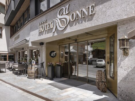 Der Eingang zum Hotel Sonne ist stilvoll gestaltet und einladend. Es gibt Sitzgelegenheiten im Freien und eine moderne Fassade.