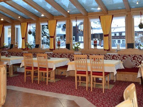 A cozy restaurant area with wooden chairs and tables. Large windows let in plenty of light and offer a view outside.