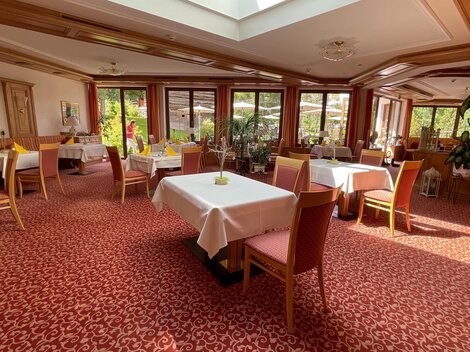 An inviting restaurant with elegant tables and red carpet flooring. Large windows provide plenty of natural light and a pleasant atmosphere.