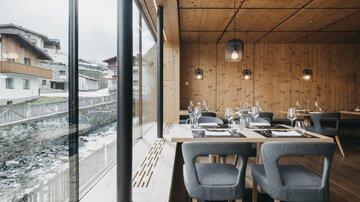 Ein modernes Restaurant mit holzverkleideten Wänden und großen Fenstern. Die Tische sind elegant gedeckt und bieten einen Blick auf die Umgebung.