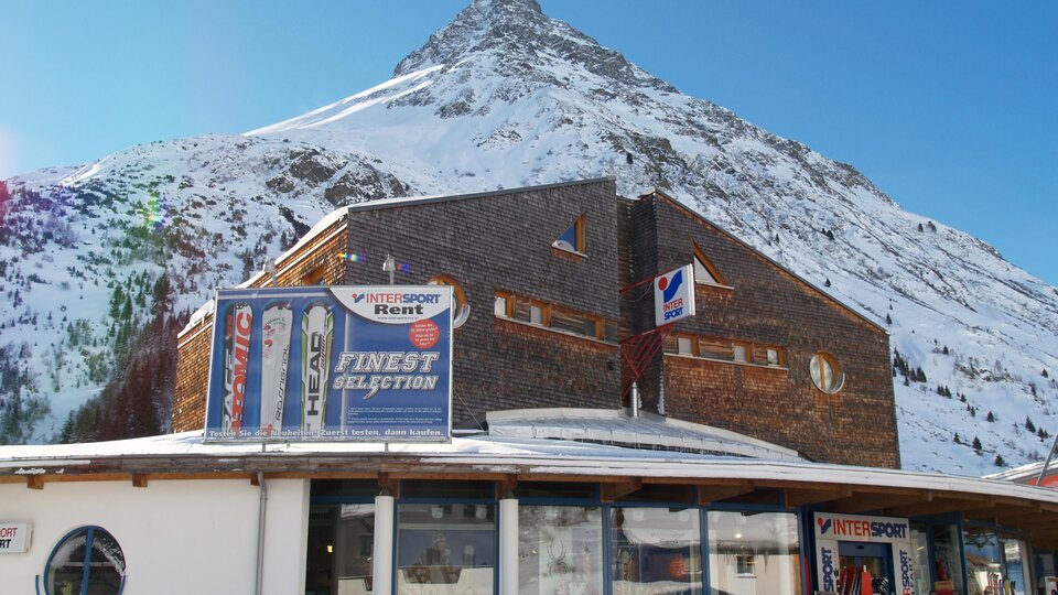 Ein modernes Gebäude vor einem schneebedeckten Berg. Der klare Himmel und die Winterlandschaft schaffen eine malerische Aussicht.