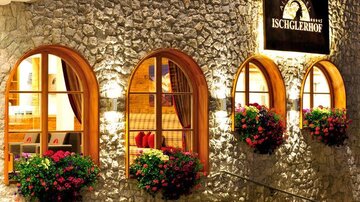 Ein gemütliches Hotel mit steiniger Fassade und großen, geschwungenen Fenstern. Blühende Blumenkästen schmücken die Fenster und verleihen dem Gebäude einen einladenden Charme.