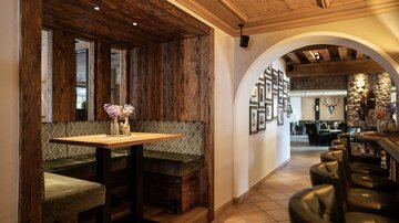 Ein gemütliches Restaurant mit Holzwänden und eleganten Sitzbereichen. Im Hintergrund sind Bilderrahmen an der Wand zu sehen und es herrscht eine einladende Atmosphäre.