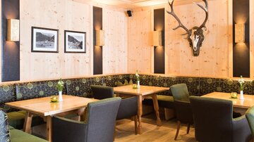 Ein gemütliches Restaurant mit Holzwänden und modernen Möbeln. An der Wand hängt ein Geweih, und die Tische sind mit frischen Blumen dekoriert.