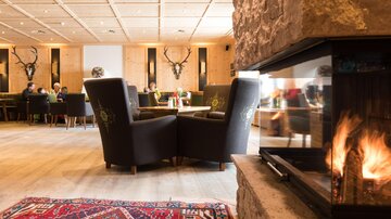 Ein gemütliches Restaurant mit eleganten Sesseln und einem offenen Kamin. Im Hintergrund sind Gäste zu sehen, die essen und sich unterhalten.