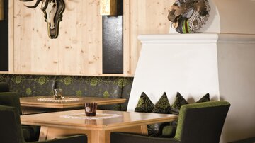 Ein stilvolles Restaurantinterieur mit Holzverkleidung und gemütlichen Sitzplätzen. An der Wand hängen ein Hirschgeweih und eine dekorative Kranzgestaltung.