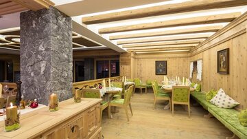Ein gemütliches Restaurant mit Holzwänden und grünen Sitzbänken. Der Raum ist hell erleuchtet und lädt zum Verweilen ein.