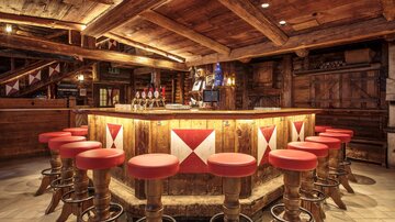 Eine gemütliche Bar mit einem runden Holztresen und roten Barhockern. Die Atmosphäre ist rustikal und einladend.