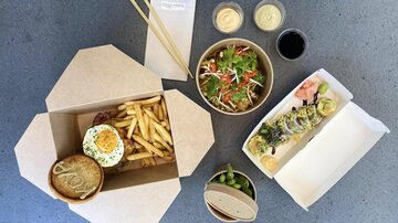 Eine appetitliche Auswahl an Essen auf einem Tisch. Es gibt Fritten, Sushi, einen Salat und verschiedene Dips in Schalen.