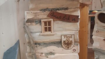 Ein rustikales Holzhaus mit einem kleinen Fenster und einem Schild mit "Grias Eich". Neben dem Fenster befindet sich das Wappen von Tirol.