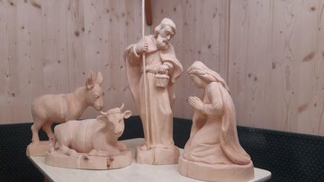 Eine Holzkrippe mit Figuren von Maria, Josef und Tieren. Die Skulpturen sind schlicht und in einem natürlichen Farbton gehalten.