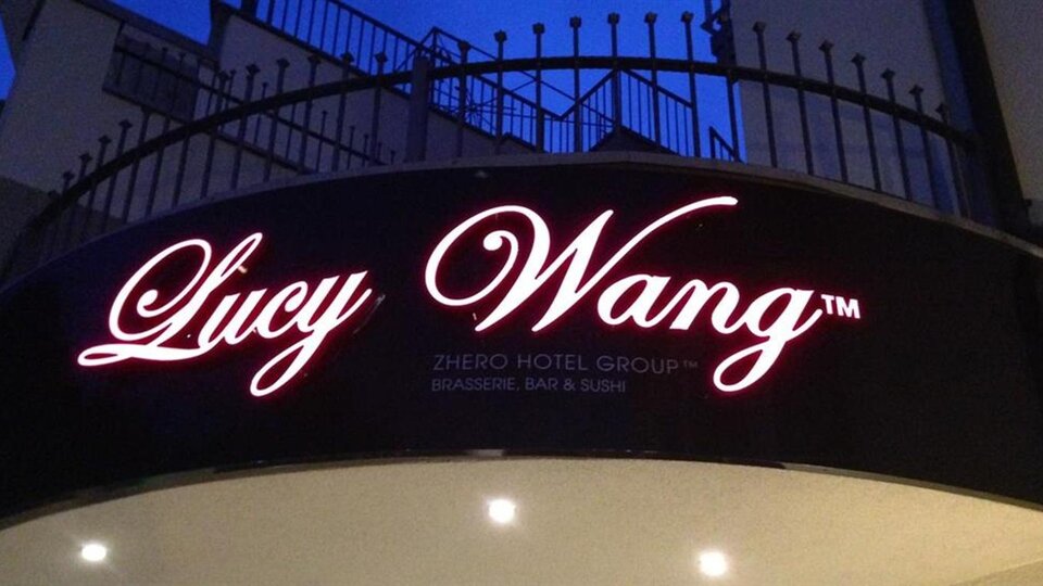 Ein Schild für das Hotel "Lucy Wang" mit einer eleganten Schriftart. Das Logo strahlt bei Nacht und zieht Aufmerksamkeit auf sich.