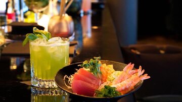 Ein köstlicher Cocktail mit frischen Kräutern steht neben einem Teller mit Sushi und Meeresfrüchten. Die farbenfrohe Präsentation auf einem eleganten Tisch lädt zum Genießen ein.
