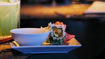 Ein Teller mit Sushi und einer kleinen Schüssel Soße. Im Hintergrund ist ein Getränk zu sehen.