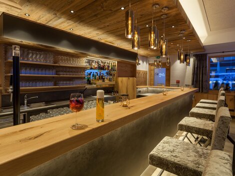 A modern bar with wooden decor and elegant lighting. In the background, there are glasses and a selection of drinks.