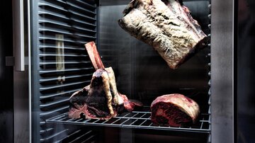 Ein Kühlschrank mit verschiedenen Fleischstücken zum Reifungsprozess. Das Fleisch ist gut sichtbar und zeigt unterschiedliche Schnitte.