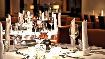 Ein elegant gedeckter Tisch in einem stilvollen Restaurant. Gläser, Besteck und dekorative Details sind sorgfältig angeordnet.