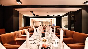 Ein eleganter Restaurantraum mit einem langen Tisch und gemütlichen Sesseln. Die Tische sind festlich gedeckt mit Gläsern und Besteck.