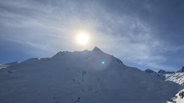 Eine verschneite Berglandschaft unter blauen Himmel. Die Sonne scheint hell über den schneebedeckten Gipfeln.