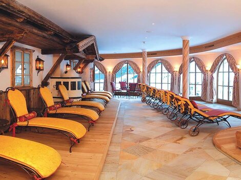 A relaxing wellness area with loungers and large windows. The cozy atmosphere is accentuated by the wooden details and soft lighting.