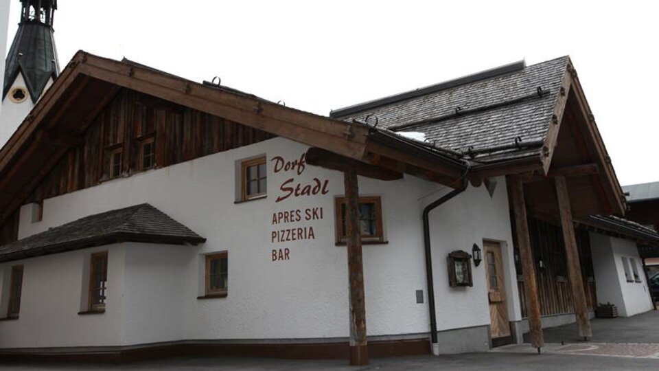 Ein gemütliches Restaurant mit Holzverkleidung, das für Après-Ski bekannt ist. Die Fassade zeigt den Namen "Dorf Stadl" und lädt zum Verweilen ein.