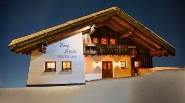 Ein traditionelles Alpenhaus mit Holzfassade und ausgebautem Dach. Es ist beleuchtet und vor einem klaren, dunklen Himmel zu sehen.