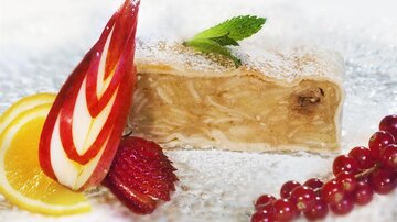 Ein köstliches Stück Apfelstrudel, garniert mit frischen Früchten und einem Minzblatt. Zartes Gebäck und eine süße Füllung machen das Dessert ansprechend.