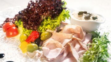 Ein Teller mit Aufschnitt, frischem Gemüse und einem Dip. Die bunte Auswahl umfasst Salat, Oliven und Tomaten.