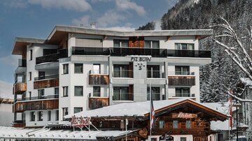 Ein modernes Hotel im Schnee, umgeben von Bergen. Der Eingangsbereich hat eine einladende Holzarchitektur.