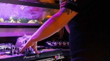 Ein DJ steuert seine Musik an einem Pioneer DJ-Setup. Die bunten Lichter schaffen eine lebendige Atmosphäre.