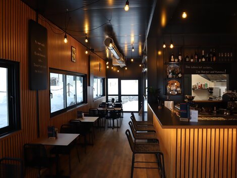 A modern café with wooden paneling and illuminated glass windows. The decor is cozy and inviting, featuring tables and chairs.