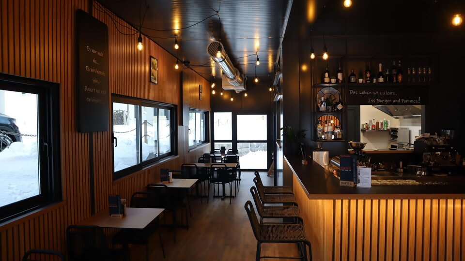 A modern café with wooden paneling and illuminated glass windows. The decor is cozy and inviting, featuring tables and chairs.