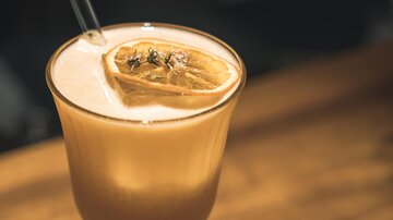 Ein erfrischendes Getränk in einem Glas mit einer Zitronenscheibe und Kräutern. Der Hintergrund zeigt eine Holzoberfläche.