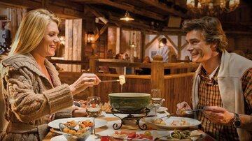 Ein gemütliches Restaurant mit einem Paar, das Fondue genießt. Auf dem Tisch liegen verschiedene Speisen und eine warme, einladende Atmosphäre.