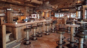 Eine rustikale Bar in einem gemütlichen Restaurant mit Holzinterieur. Es gibt hohe Tische und Stühle, die ein einladendes Ambiente schaffen.