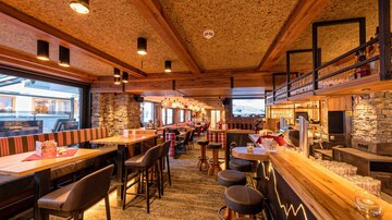 Eine gemütliche Bar mit Holzinterieur und warmem Licht. Die Sitzplätze laden zum Entspannen und Genießen ein.